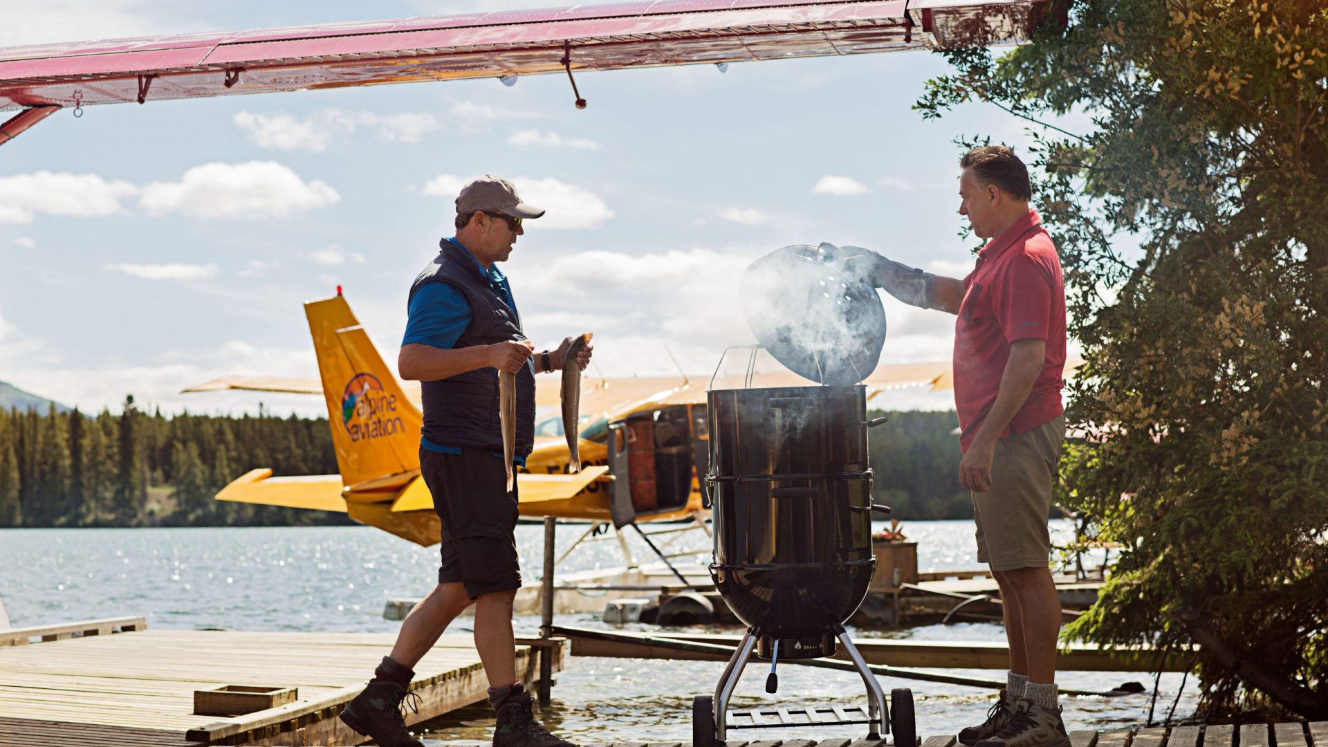 Rösle Fotoshooting mit einem Grill im Yukon. Im Hintergrund Wasserflugzeug.