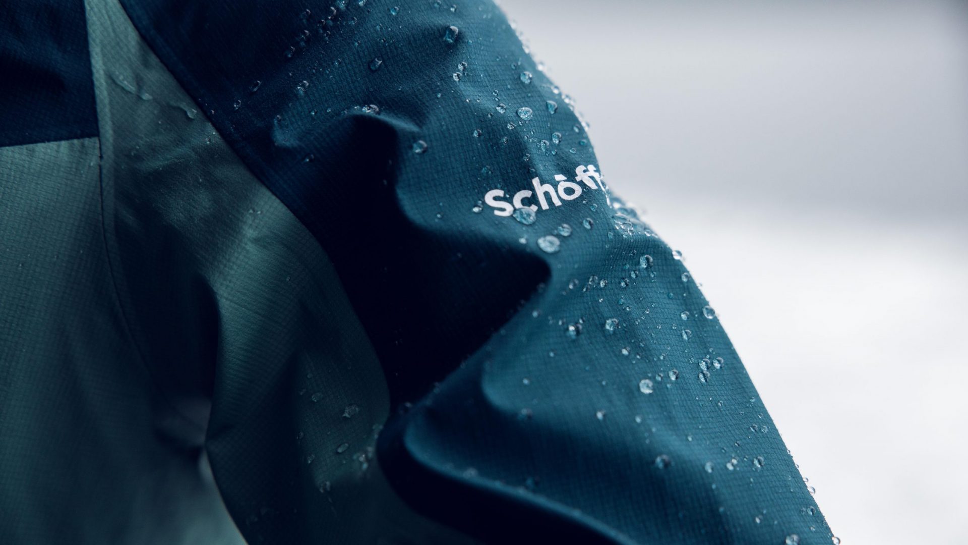 Regentropfen auf einer Funktionsjacke mit Schöffel-Logo.